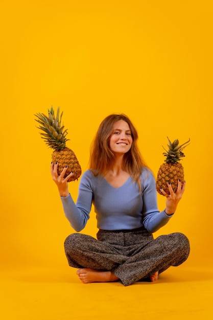 Mujer vegetariana sonriendo con una piña cortada sentada en un espacio de copia de fondo amarillo