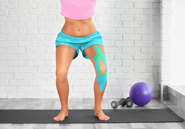 Mujer con vendaje elástico en la rodilla haciendo ejercicios deportivos en el gimnasio