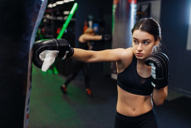 Mujer en vendas de boxeo negro y ropa deportiva golpea un saco de boxeo, box training. Boxeadora en gimnasio, kickboxer chica en club deportivo, práctica de golpes