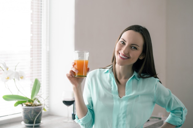 Mujer en la ventana de la cocina, sonriendo y sosteniendo un vaso de jugo