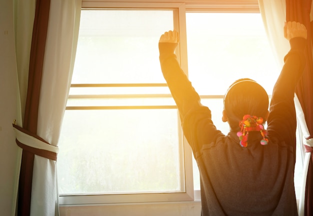 Mujer en la ventana levantando las manos frente a la salida del sol en la mañana, se despierta en la mañana con sunrise.dream suave style.feeling fresco, feliz y disfrutar