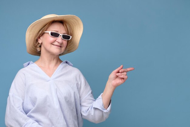 Mujer en verano sombrero y gafas de sol apuntando a un lado con gran humor sonriendo