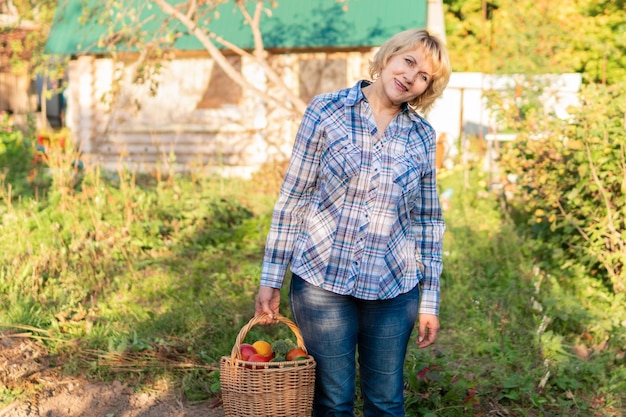 Mujer con verduras frescas en una cesta en el jardín en otoño