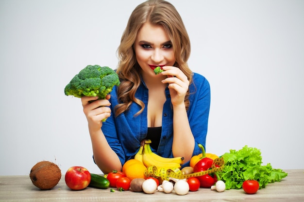 Mujer con verduras y frutas frescas sobre fondo de pared blanca.