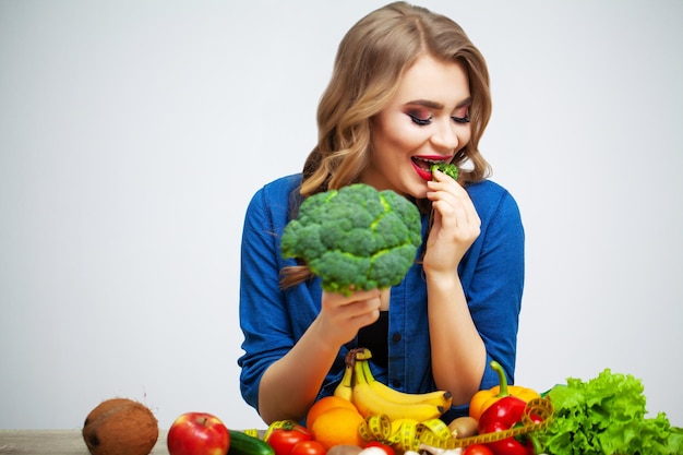 Mujer con verduras y frutas frescas sobre fondo de pared blanca.