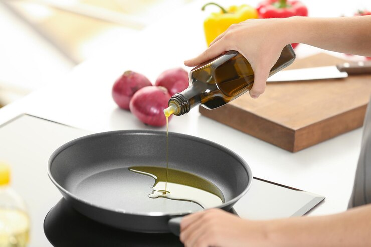 Foto mujer vertiendo aceite de cocina de la botella en la sartén sobre la estufa