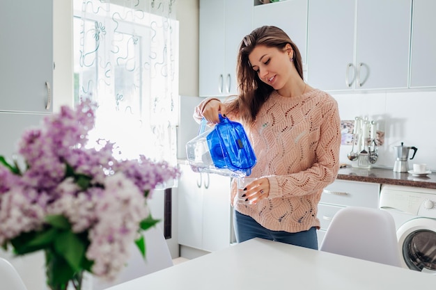 Mujer vertiendo agua filtrada de la jarra del filtro en el vaso en la cocina cocina moderna diseño vida saludable