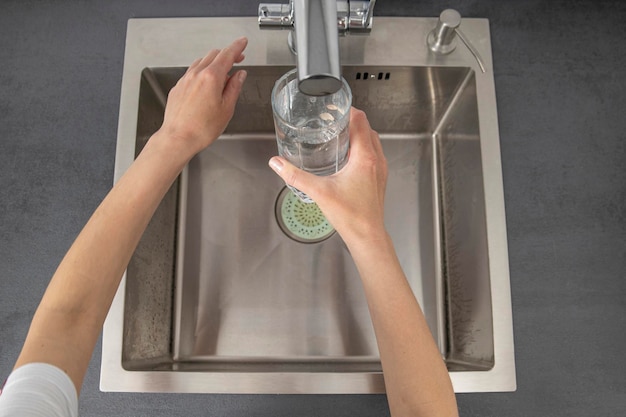 Mujer vertiendo agua en un vaso en la cocina Vista superior plana
