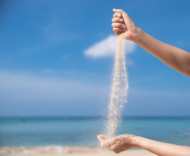 Mujer vertiendo la arena de mano en mano en la playa, cielo azul.