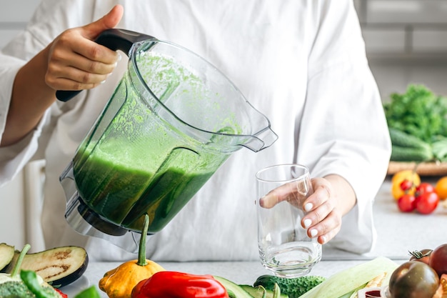 Una mujer vertiendo batido verde en un vaso concepto de comida saludable