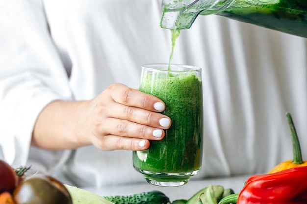 Una mujer vertiendo batido verde en un vaso concepto de comida saludable