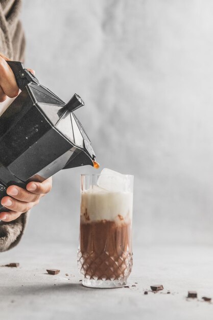 Foto mujer vertiendo café con la cafetera de moka en un vaso con mocha helada en la mesa