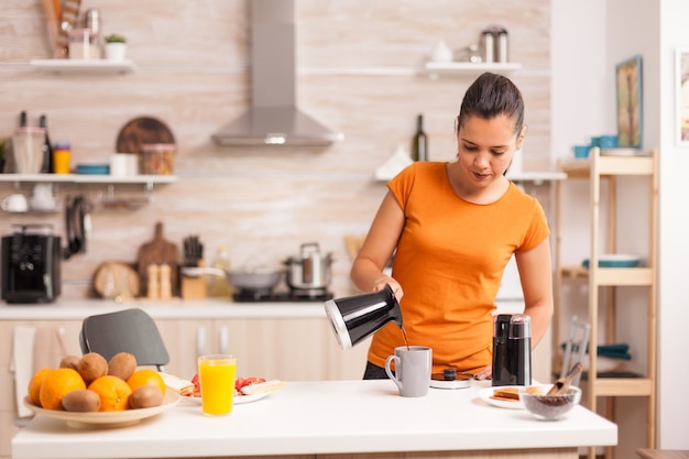 Mujer vertiendo café caliente en la taza por la mañana de la olla