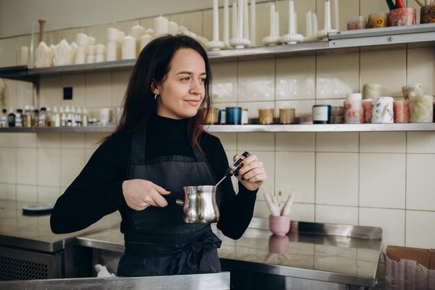 Mujer vertiendo cera derretida en un recipiente de velas ámbar Negocio ecológico y vegano Accesorios para velas de cera de soja Hecho a mano con amor Trabajo remoto Tienda en línea lugar de trabajo