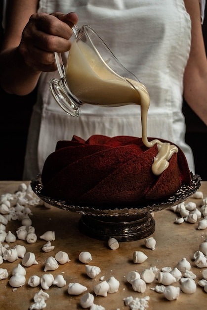 Foto una mujer vertiendo crema en un pastel de chocolate.