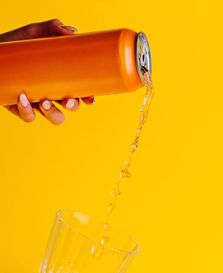 Mujer vertiendo jugo de naranja de lata en un vaso sobre un fondo amarillo