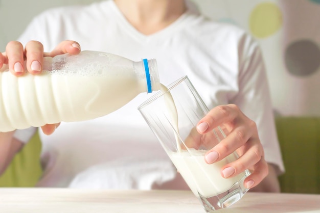 Foto una mujer está vertiendo leche de la botella en un vaso sentada en la mesa en la cocina