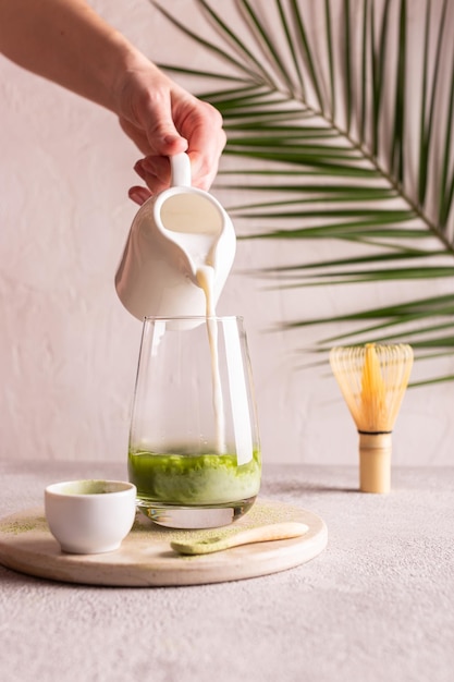 Foto mujer vertiendo leche en un vaso con matcha de té verde