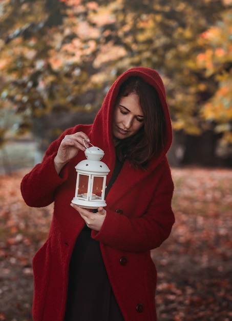 Mujer vestida con un abrigo burdeos sosteniendo una linterna en el bosque de otoño estilo victoriano vintage