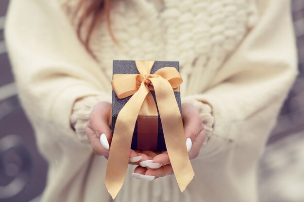 Mujer vestida con un abrigo de invierno sosteniendo una pequeña caja de regalo con un lazo de seda en la calle