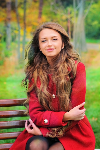 Mujer vestida con abrigo rojo sentado en el parque de otoño.