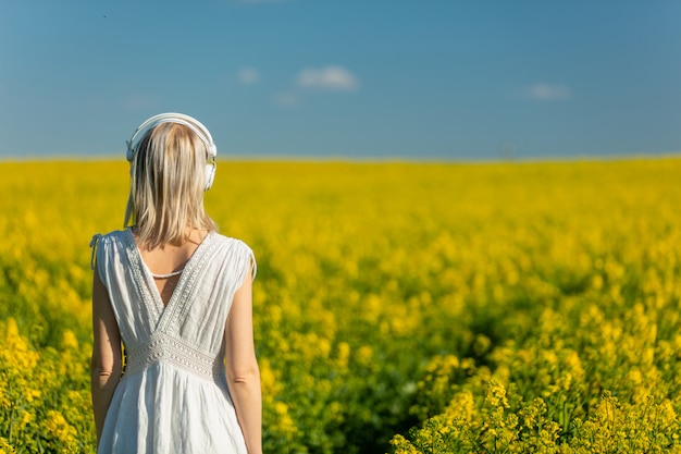 Mujer vestida con auriculares en campo de colza