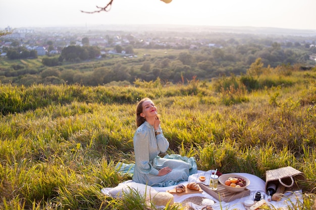 Una mujer vestida de azul se sienta en un picnic en un parque con vista panorámica