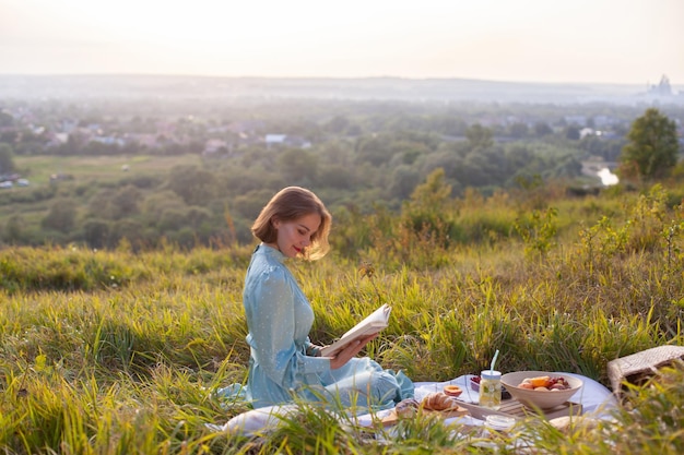 Una mujer vestida de azul se sienta en un picnic en un parque con vista panorámica