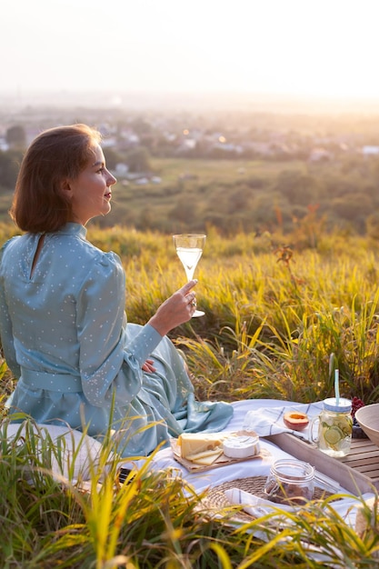 Una mujer vestida de azul se sienta en un picnic en un parque con vista panorámica