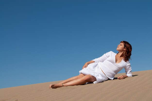 Mujer vestida de blanco disfrutando de las dunas de arena en un soleado día de primavera o verano