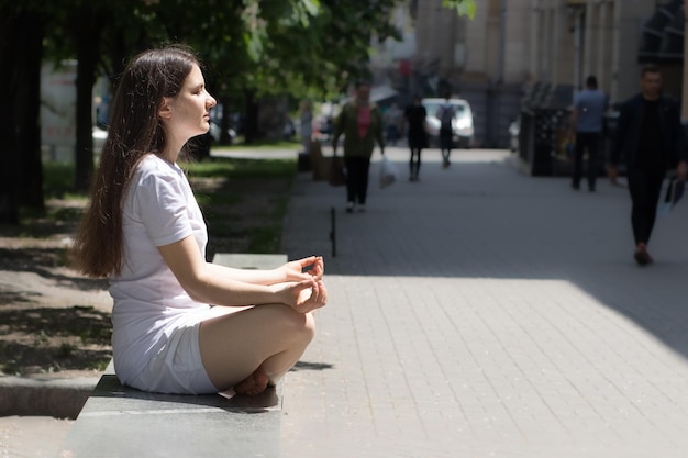 Mujer vestida de blanco medita en la calle de la ciudad.