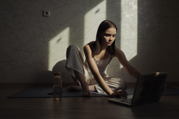 mujer vestida de blanco usando una laptop y viendo lecciones en línea durante una sesión de yoga