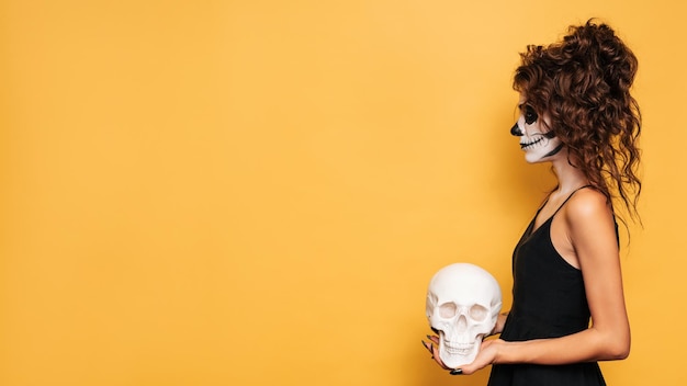 mujer vestida con un disfraz de Halloween con maquillaje para las vacaciones en el fondo con calavera en la mano