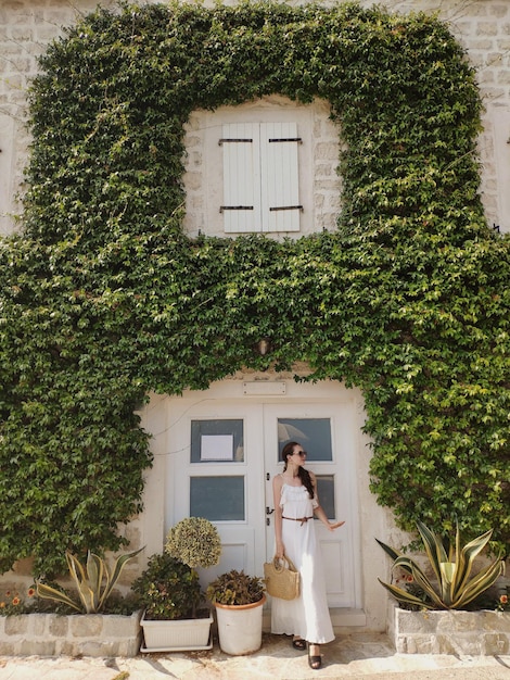 Mujer vestida está parada cerca de un edificio cubierto de plantas en el casco antiguo de Perast