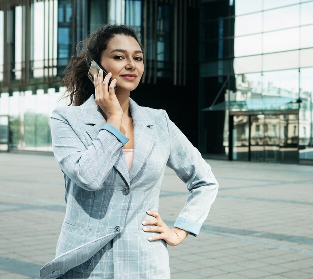 Mujer vestida con estilo de negocios en el contexto de un centro de negocios sostiene un teléfono móvil