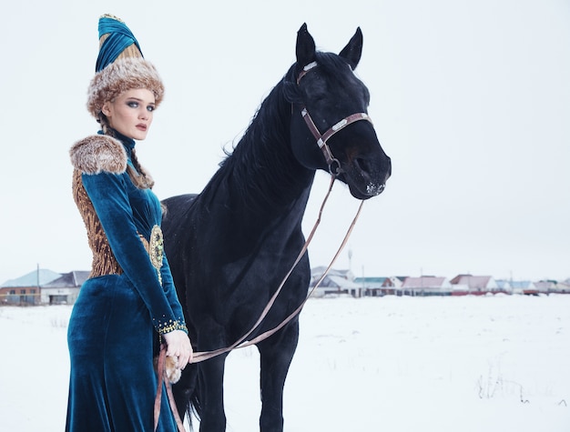 Foto mujer vestida con un hermoso vestido en paisaje invernal con caballo
