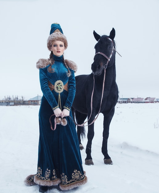 Foto mujer vestida con un hermoso vestido en paisaje invernal con caballo