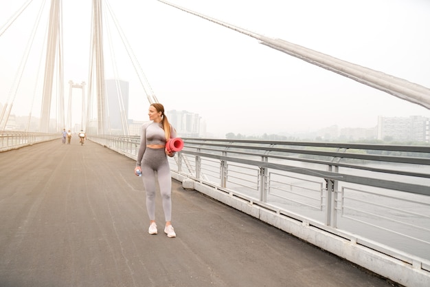 Mujer vestida con leggings y top con tapete rosa haciendo yoga en verano. fondo urbano. Concepto de estilo de vida deportivo saludable. Ejercicios femeninos activos y atléticos.