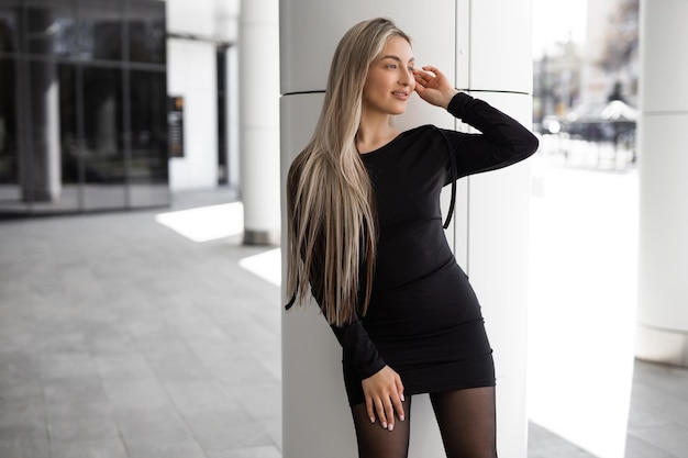 Una mujer vestida de negro se apoya en una columna blanca.