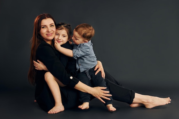 Foto una mujer vestida de negro con estilo está con su pequeño hijo y su hija en el estudio