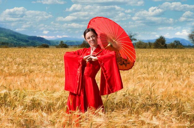 Mujer vestida de rojo con paraguas chino posando en el campo de trigo