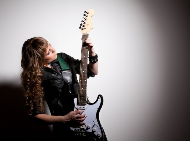 Mujer vestida con ropa de cuero negro, en cuclillas y agarrando su guitarra. Cabeza girada hacia los lados