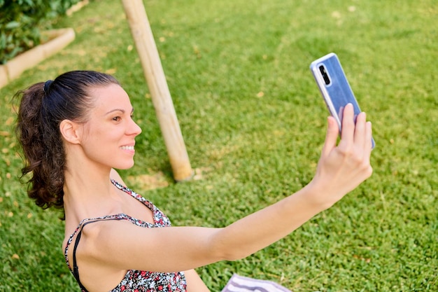 Mujer vestida sonriendo tomándose un selfie en el césped