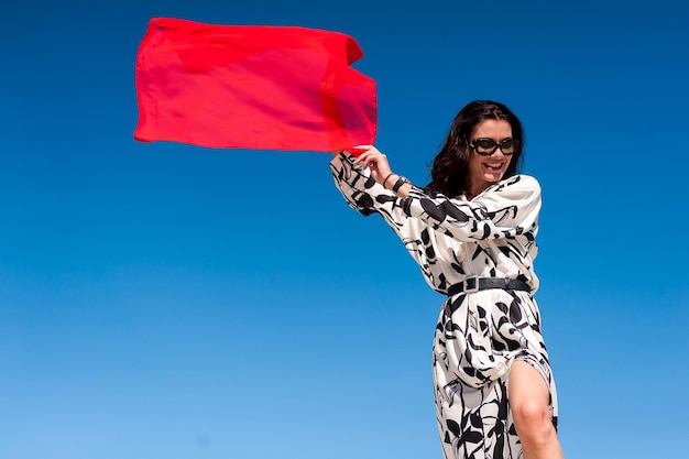 Una mujer vestida sostiene una bandera roja frente a un cielo azul.