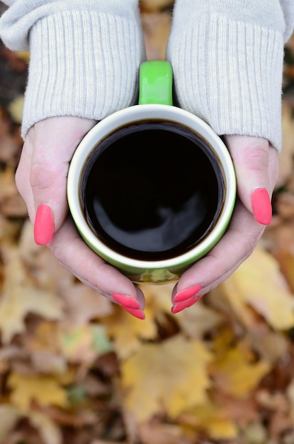 Mujer vestida con suéter blanco sosteniendo una taza de café verde