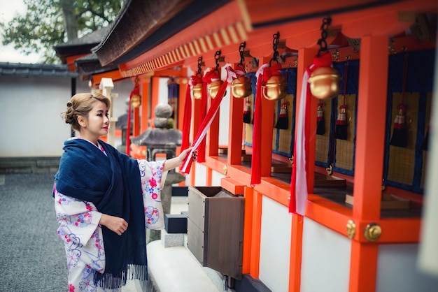 Mujer vestida con traje tradicional japonés caminando bajo las puertas tori en el santuario fushimi-inari, Kioto, Japón