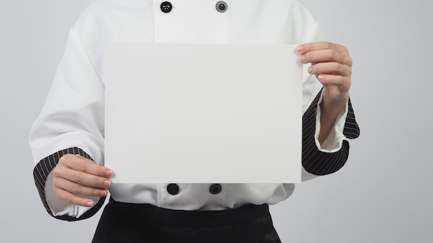 Foto mujer vestida con uniforme de chef y sosteniendo papel a4 sobre fondo blanco.