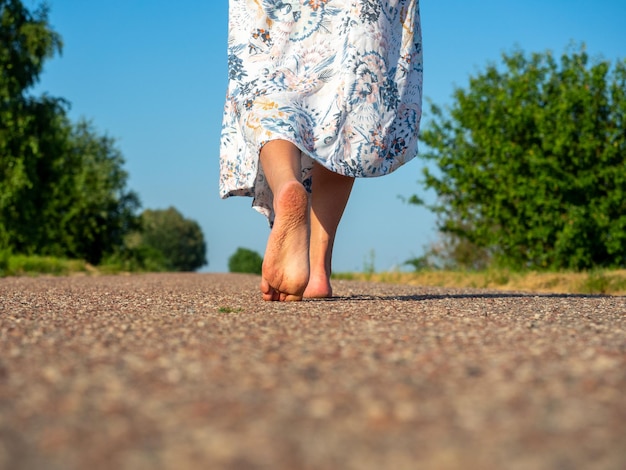 Una mujer vestida con un vestido camina descalza sobre el asfalto Vista trasera El concepto de viajes recreación vacaciones libertad