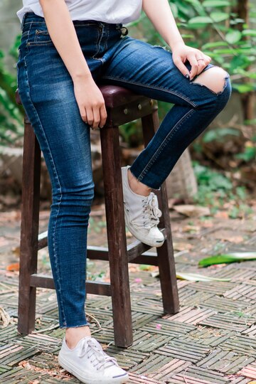 Mujer con zapatillas blancas, jeans y una camiseta blanca sentada en una silla de madera. Foto Premium