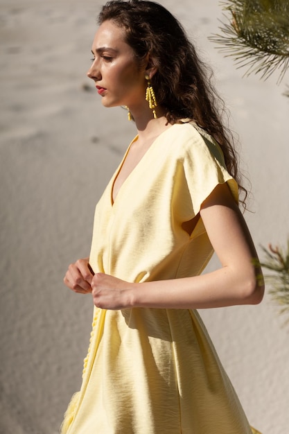 Una mujer con un vestido amarillo se para en la arena.